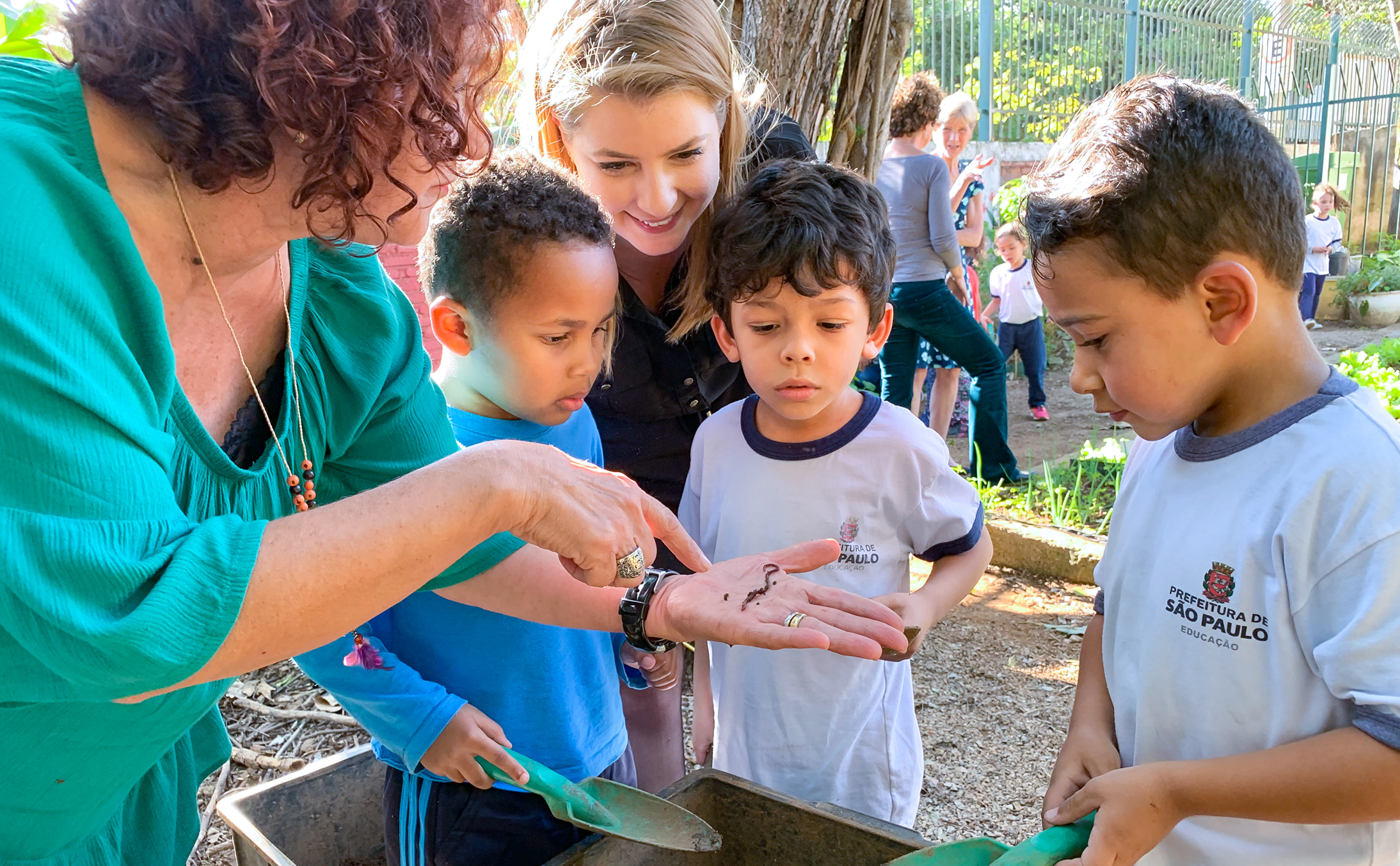 Teacher shows preschool students a worm in outdoor classroom.