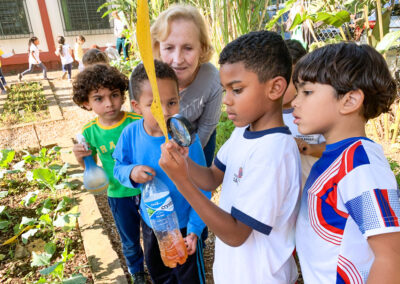 Preschool students and teacher examine leaf with a magnifying glass.