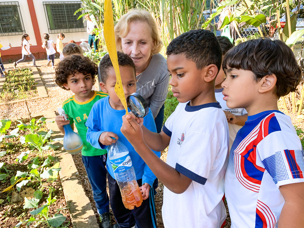 Preschool students and teacher examine leaf with a magnifying glass.